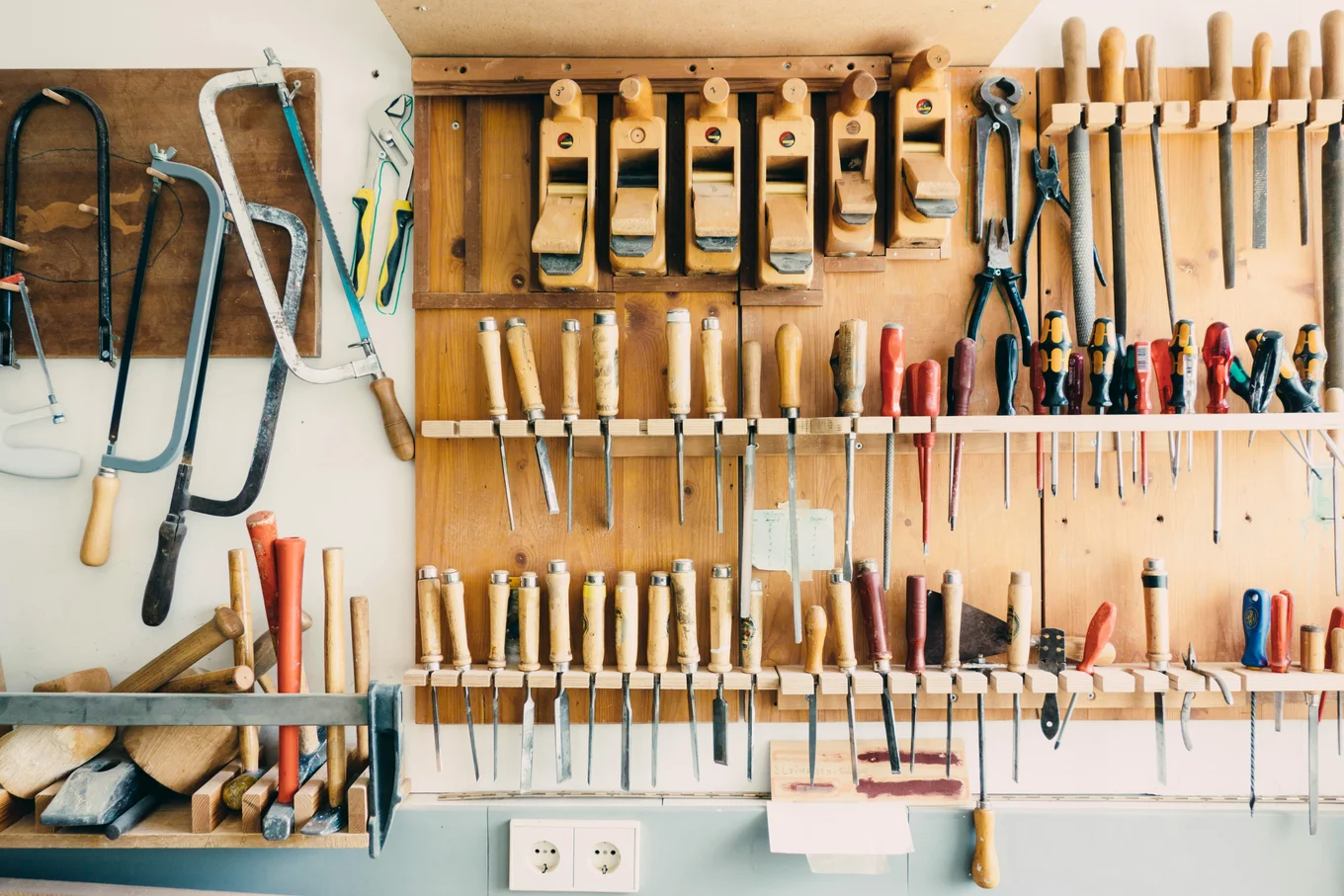Various hand tools organized on a wooden wall rack.